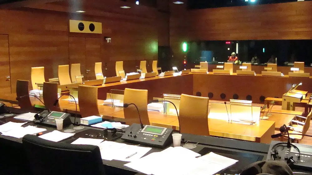 The view from an interpreting booth at the Court of Justice of the European Union in Luxembourg: consoles, microphones and a headset in the foreground, the empty courtroom beyond the glass